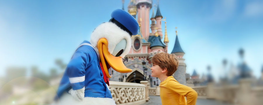 Young boy with donald duck by sleeping beauty castle.