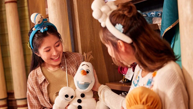 Guests shopping in Fjord View Shop trying on headbands and playing with Olaf toy.