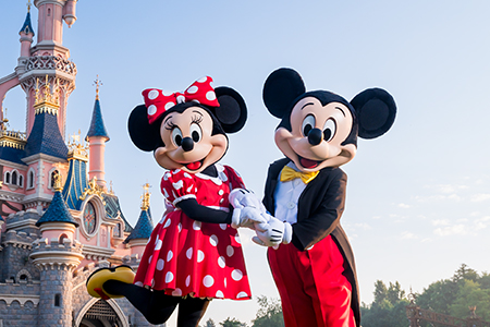 Mickey Mouse and Minnie Mouse holding hands and posing in front of Sleeping Beauty Castle