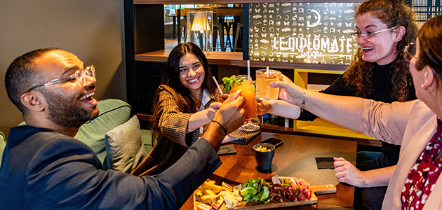 Four friends raising their glasses together with a sharing platter at Le Diplomate, the bar at H&ocirc;tel l'Élys&eacute;e Val d'Europe.