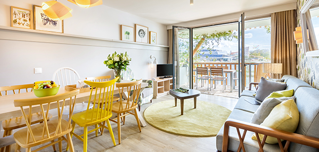 Living space of a Premium Apartment at Les Villages Nature Paris, featuring a dining table, sofa, TV and balcony