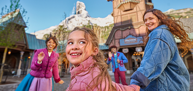 Excited Guests  holding hands while walking through World of Frozen at Disney Adventure World, with Cast Members waving in the background.