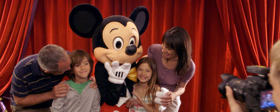 Mickey Mouse posing with a family, having a photo taken by a Disney PhotoPass photographer