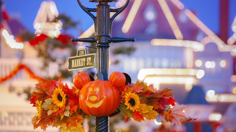 Street lamp on Main Street at Disneyland Paris decorated with a carved Mickey-shaped pumpkin, sunflowers and orange autumn leaves