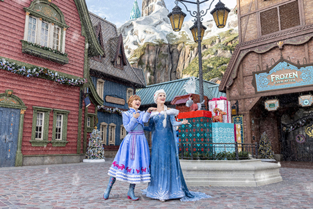 Elsa and Anna standing in the snow at World of Frozen, with the North Mountain and the Frozen Ever After attraction in the background